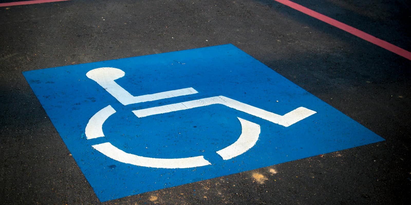 A white wheelchair accessibility symbol painted on a blue square on asphalt