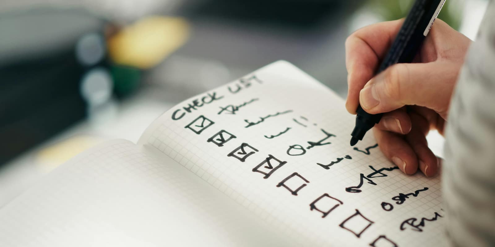 A hand ticking items off a handwritten checklist in a notebook