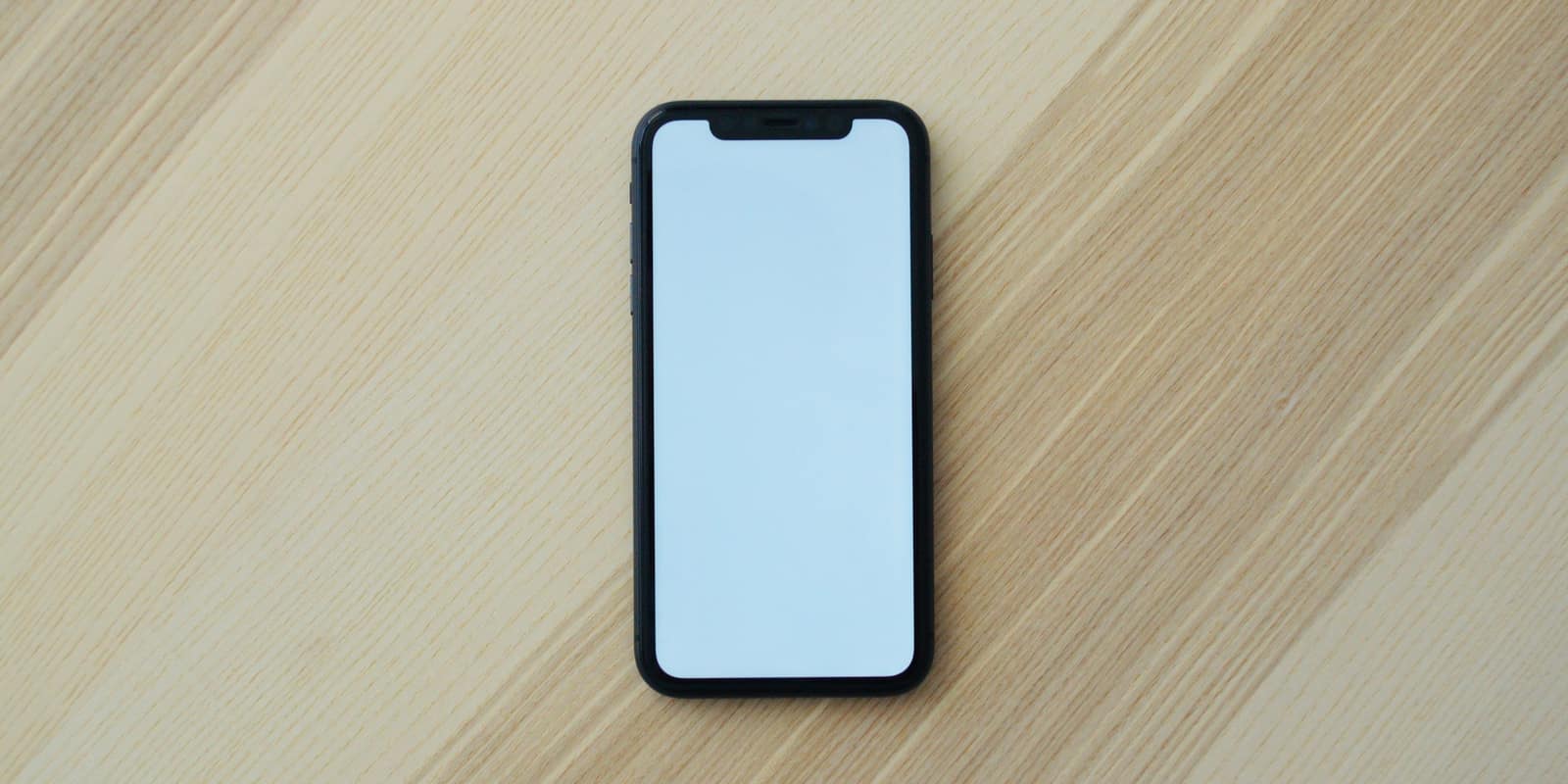 A black smartphone with a blank white screen on a light wooden surface