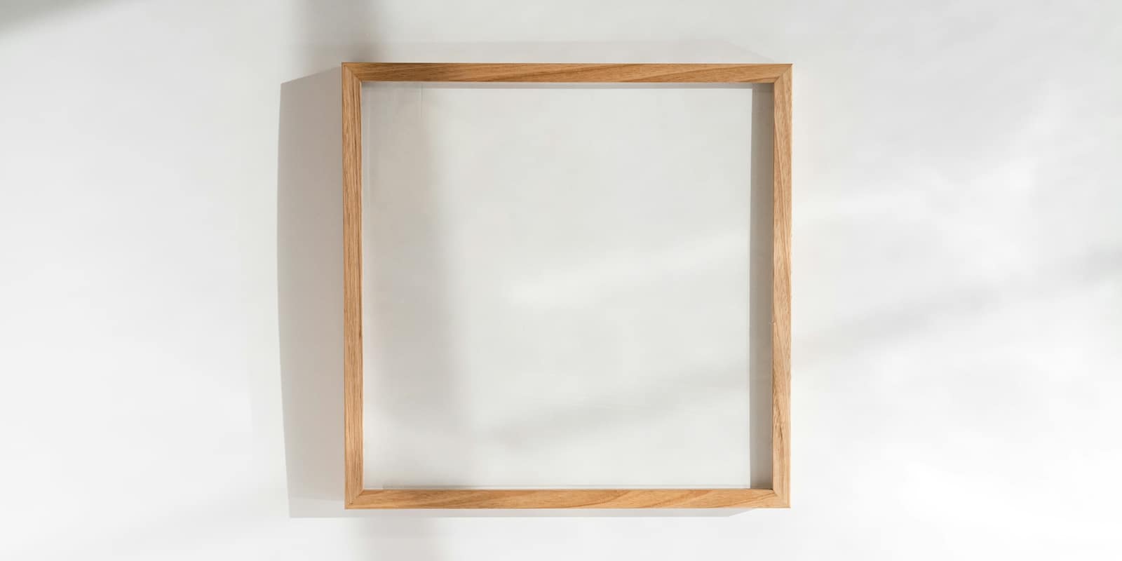An empty square wooden frame hanging on a white wall