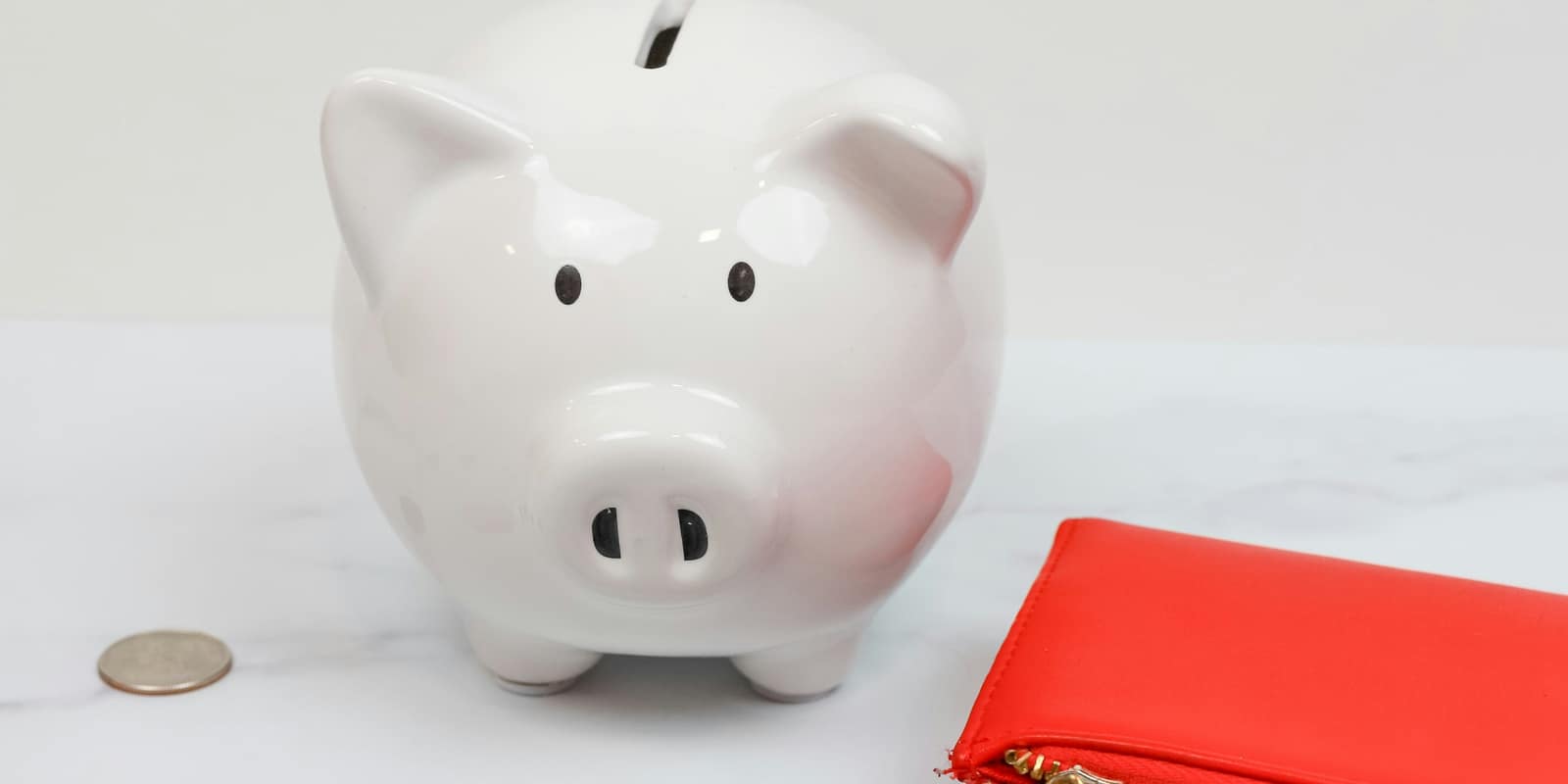 A white piggy bank beside a single coin and a red wallet