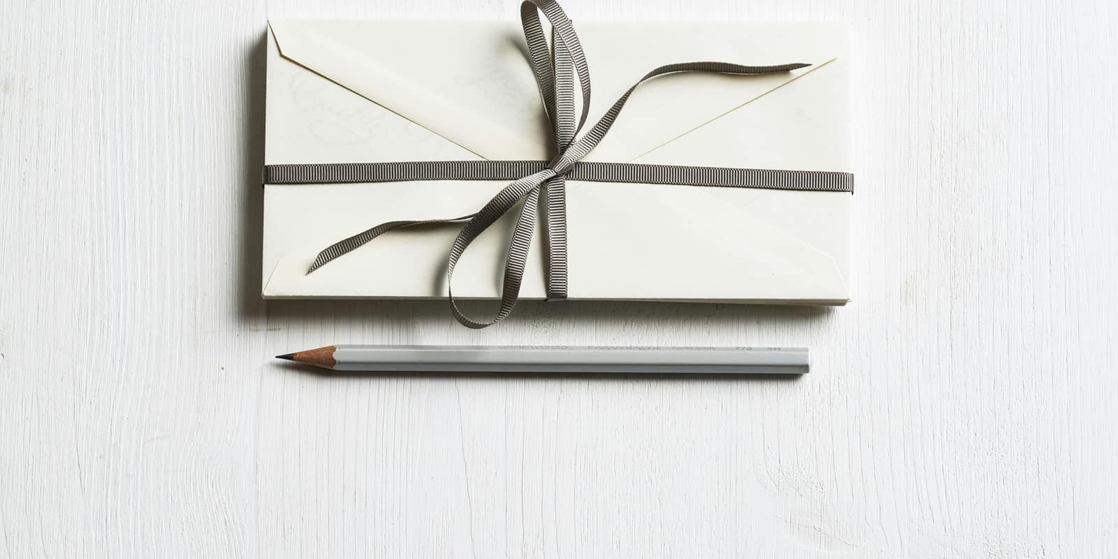 A white envelope tied with grey ribbon above a pencil on a white desk