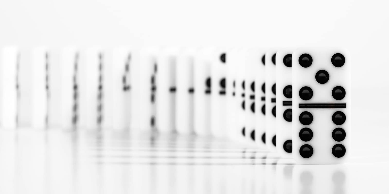 A long row of white dominoes standing on a white surface