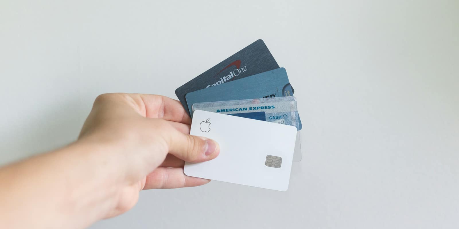 A hand holding several payment cards fanned out against a white wall