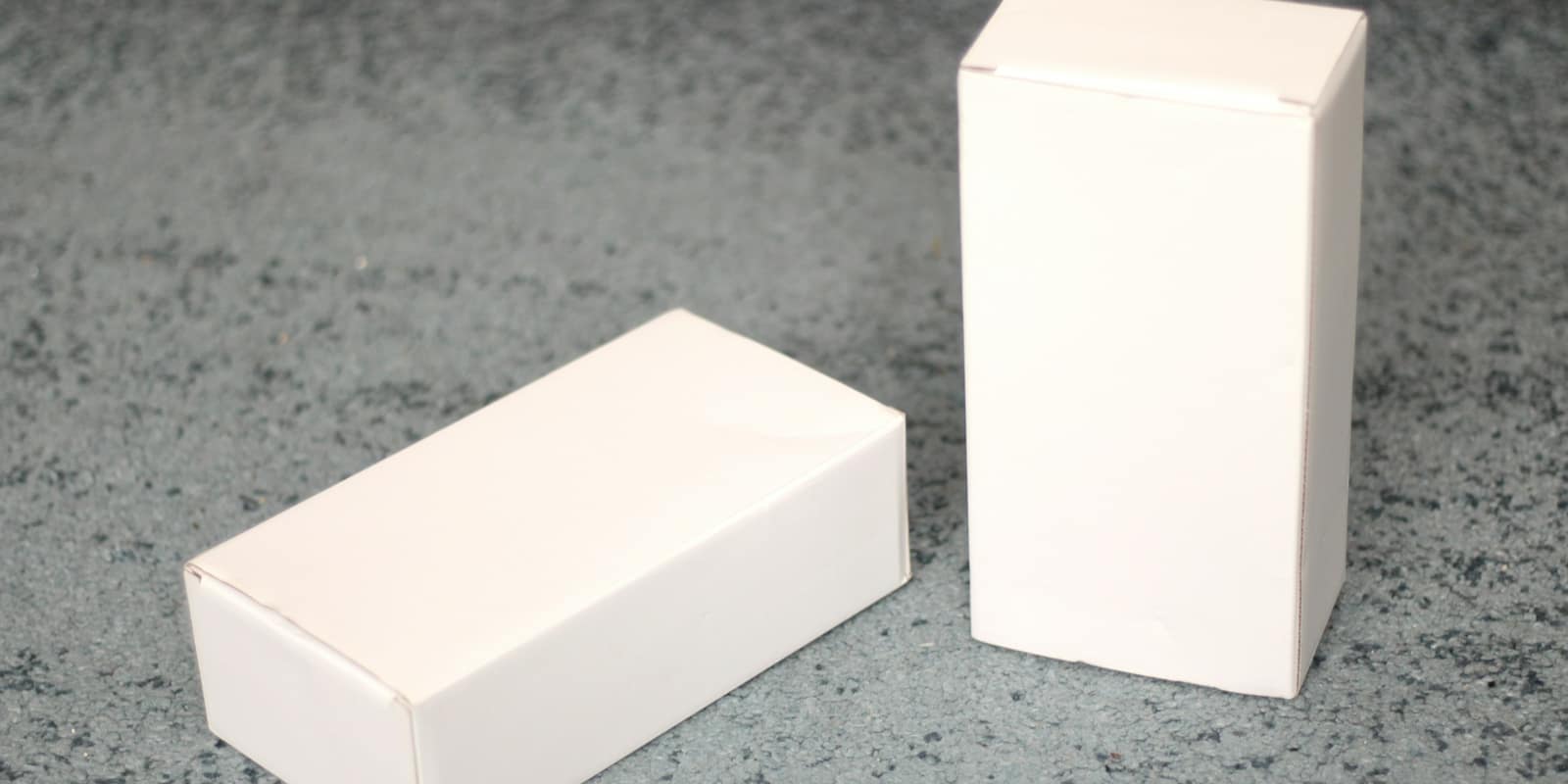 Two white boxes on a grey stone surface, one lying down and one standing