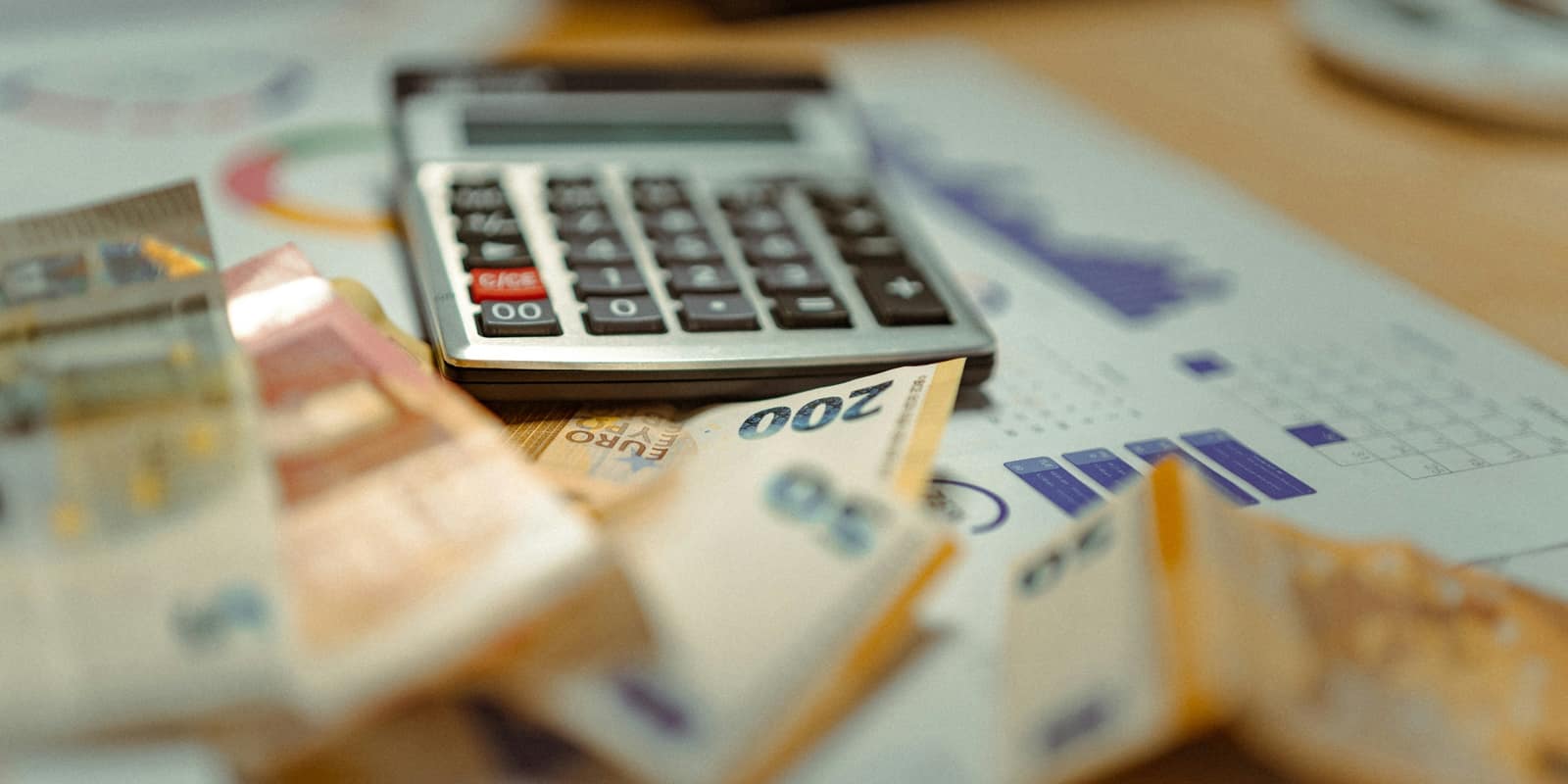 A calculator on charts beside folded banknotes